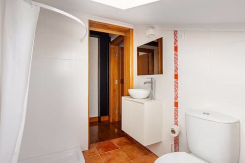 Modern bathroom at Casa dos Vasconcelos cottage in Chaves with white tiles, wooden accents, vessel sink, and terracotta floor