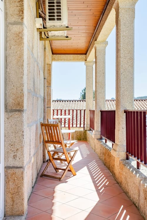 Sunny terrace at Casa dos Vasconcelos cottage in Chaves with wooden chair, stone columns, and red rooflines