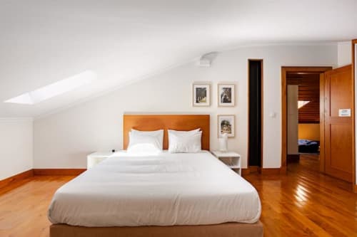 Modern attic bedroom at Casa dos Vasconcelos cottage in Chaves with wooden bed, white bedding, skylights, and hardwood