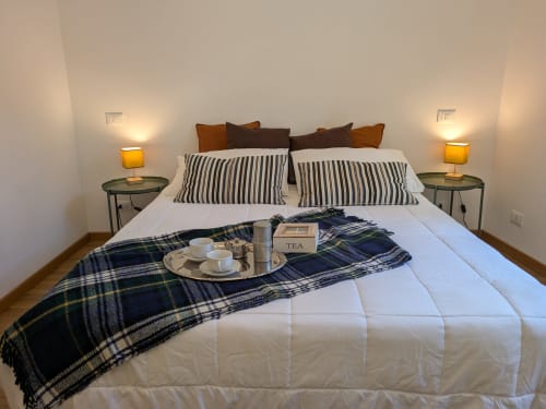 Elegante letto matrimoniale con cuscini rigati, plaid scozzese, servizio da tè e lampade calde nella camera del B&B di Palermo