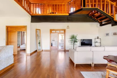 Spacious Casa dos Vasconcelos cottage living room in Chaves with wooden loft, TV, white furniture, and hardwood floors