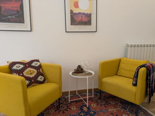 Poltrone giallo brillante con cuscini geometrici di fronte a un tavolino bianco nella camera di un B&B a Palermo, con arte da viaggio alle pareti