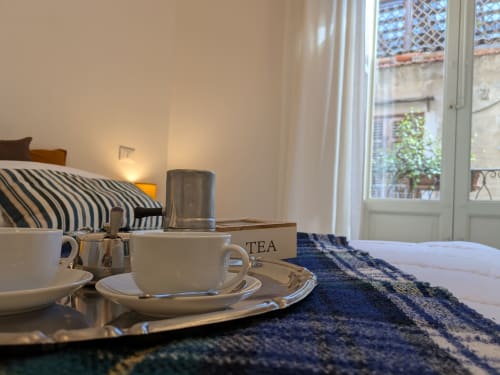 Servizio da tè sul letto della camera BnB a Palermo con cuscini a righe e porte balconate con vista sulla città
