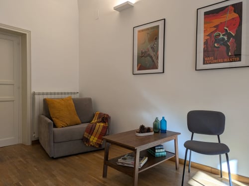 Zona living moderna nel B&B di Palermo con poltrona grigia, tavolo in legno, poster incorniciato dell'esploratore di Marte e cuscino accent giallo