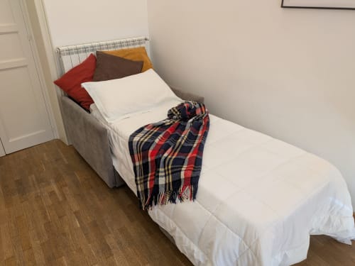 Camera accogliente con biancheria bianca e plaid nel BnB del Parlamento Palermo, cuscini colorati, pavimento in legno e termosifone