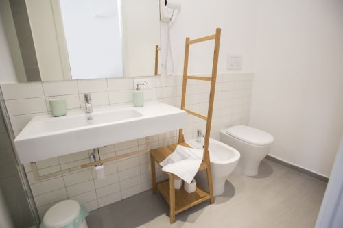 Bagno moderno presso BnB del Parlamento Palermo con piastrelle bianche, lavabo, wc, scaletta in legno per asciugamani e accenti verde menta