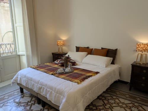 Elegante camera da letto presso BnB del Parlamento Palermo con biancheria bianca, cuscini marroni, comodini in legno e vista sulla città