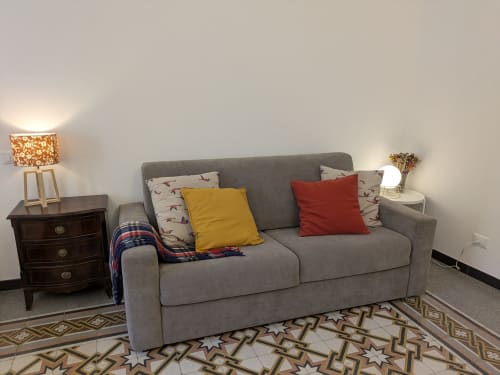 Accogliente soggiorno del BnB del Parlamento Palermo con divano grigio, cuscini decorativi, comodino in legno e motivo geometrico