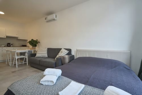 Moderno monolocale a Rozzano con letto, divano grigio, angolo cottura, climatizzazione e asciugamani bianchi