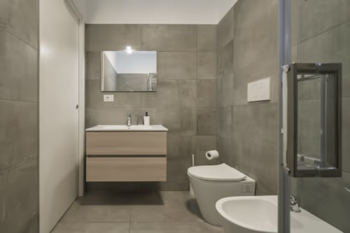 Bagno moderno dell'appartamento AirFlat a Rozzano, con piastrelle grigie, mobile in legno con lavabo, bidet e doccia