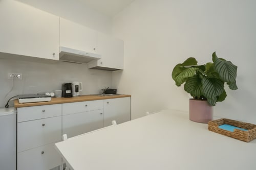 Cucina moderna bianca con piano di lavoro in legno, pianta rosa in vaso e zona pranzo nell'appartamento AirFlat a Rozzano