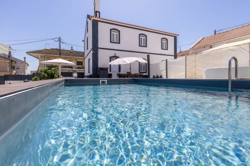 Alojamento CSA pool in Camarnal with blue water, white umbrellas, and Portuguese architecture building.