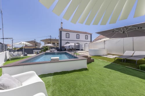 Alojamento CSA pool area in Camarnal with loungers, umbrellas, and white pergola overlooking traditional Portuguese building
