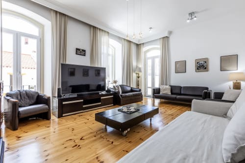 Modern spacious living room at Alojamento CSA in Camarnal with wooden floors, dark leather furniture, TV, and bright windows