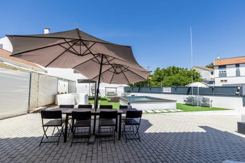 Alojamento CSA patio with dining table, umbrellas, pool, and green lawn in Camarnal, Portugal