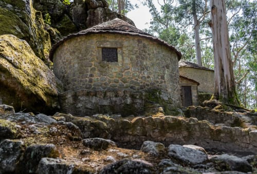 Casarão de pedra com telhado cônico entre rochas cobertas de musgo e eucaliptos no House Park, Esposende Portugal