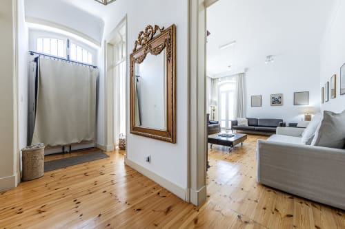 Foyer luminoso do Alojamento CSA com piso de madeira, espelho ornamentado e vista para sala de estar com mobiliário cinzento