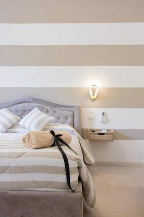 Camera minimalista a La Maison Du Lion B&B a La Spezia con pareti a righe beige, testata trapuntata e calda illuminazione comodino