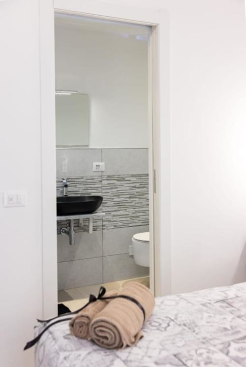 Bagno en-suite moderno con parete di piastrelle rigate, lavabo nero a bacinella e wc bianco, accesso dalla camera doppia Luna