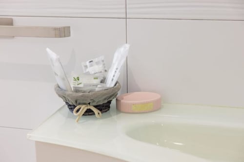 Il bancone del bagno di La Maison Du Lion con cestino di articoli da toilette e barattolo rosa nella camera Vittoria, La Spezia
