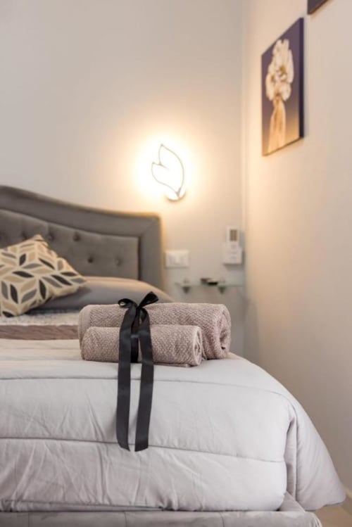 Elegante camera da letto a La Maison Du Lion con asciugamani arrotolati legati con nastro nero su biancheria bianca, testata rivestita in grigio