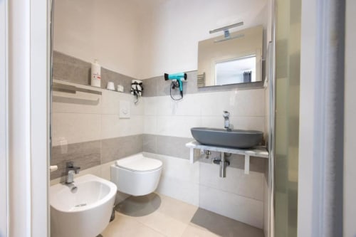 Bagno moderno della camera Perla di La Maison Du Lion con piastrelle grigie, bidet, toilette e lavabo grigio con specchio