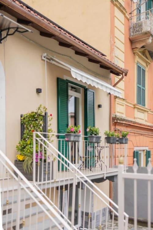Camera doppia Luna con balcone a La Maison Du Lion a La Spezia: persiane verdi, ringhiera bianca, fiori in vaso e vista città