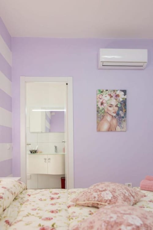 Camera luminosa di La Maison Du Lion con pareti lavanda, biancheria floreale e aria condizionata a La Spezia