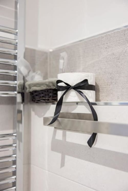 Elegante portasciugamani da bagno con asciugamani bianchi arrotolati legati con nastro nero presso La Maison Du Lion B&B a La Spezia