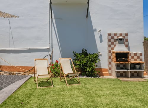 Patio soleado con tumbonas, jardín verde y chimenea de ladrillos decorativos en la villa Alhaurín Loft