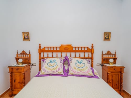 Cama de madera con cabecera ornamentada y ropa de cama púrpura en la villa Riad de Alhaurín, flanqueada por mesitas de noche