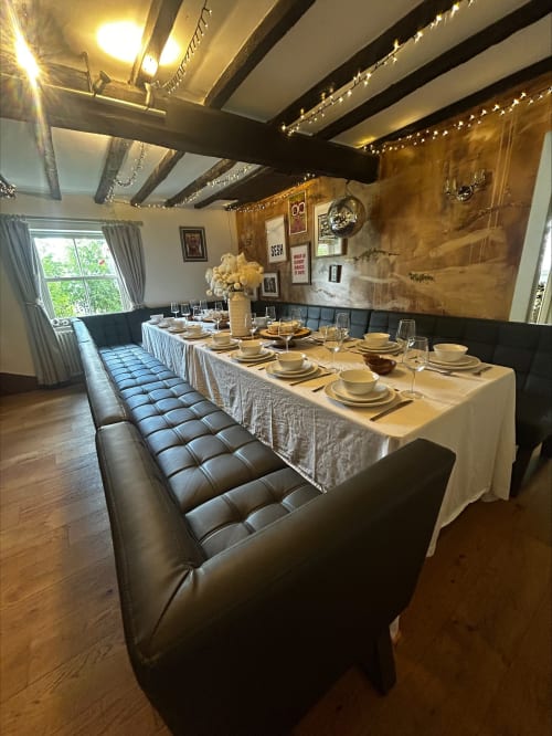 Elegant dining room at The Lavender House with long table, black leather banquette seating, cream linens, and exposed beams
