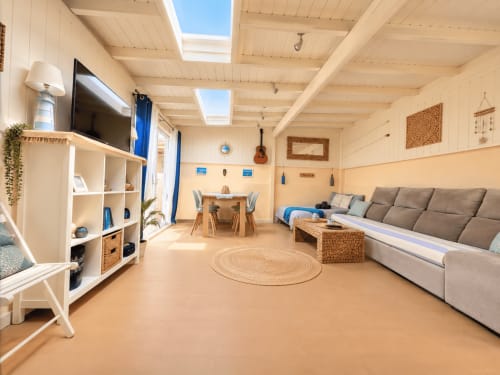 Luminoso appartamento open space a Corralejo con lucernai, divano grigio, scaffali bianchi, zona pranzo e tappeto rotondo