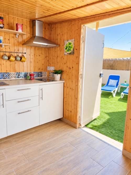 Cucina moderna in legno con armadietti bianchi che si affacciano su un patio soleggiato con lettini presso S & G House Corralejo