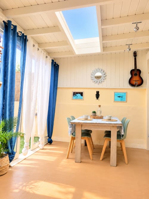 Sala da pranzo luminosa nell'appartamento S & G House Corralejo con tavolo in legno, tende blu, lucernari e decorazione a forma di chitarra a parete