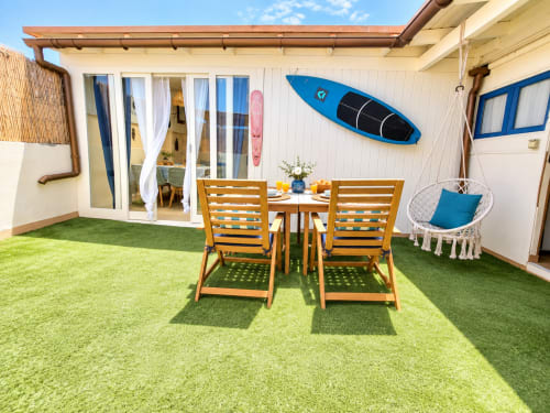 Terrazza fronte mare a Sara & Gino Fuerteventura con tavolo da pranzo, lettino, erba sintetica, tavole da surf e poltrona sospesa a uovo