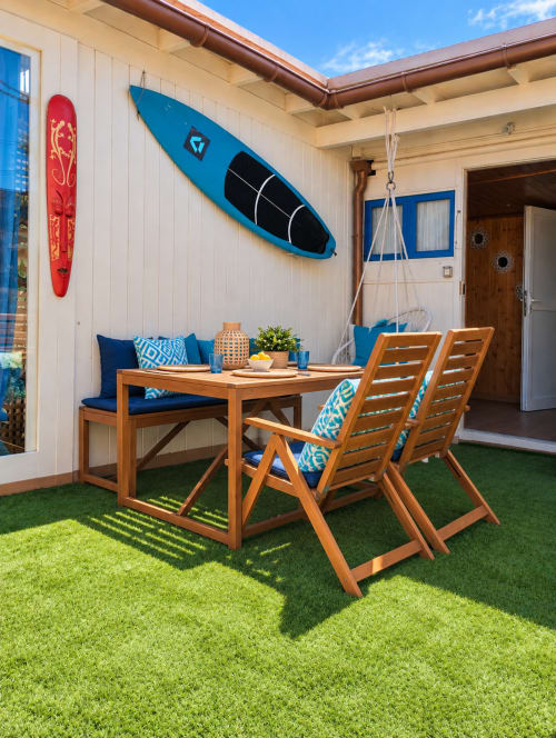 Patio fronte mare presso Sara & Gino Fuerteventura con tavolo da pranzo in legno, sedie imbottite blu, tavole da surf e prato sintetico