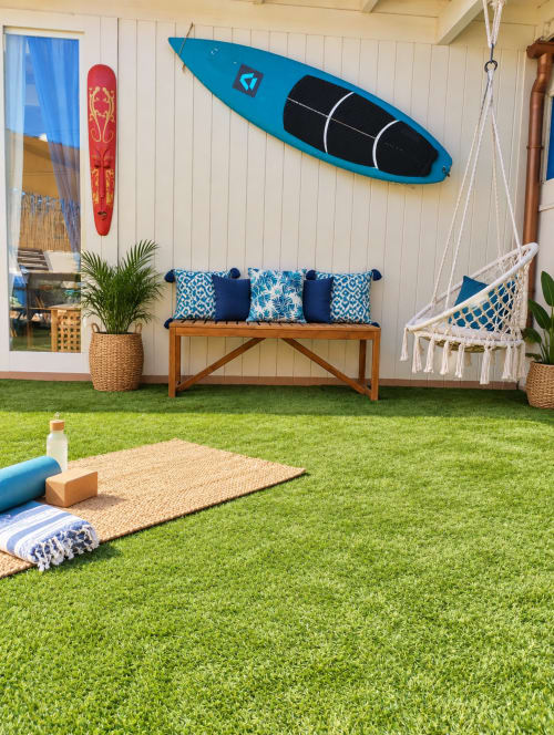 Interno di appartamento fronte mare con tappetino yoga, panca in vimini con cuscini blu, tavole da surf e amaca a Corralejo