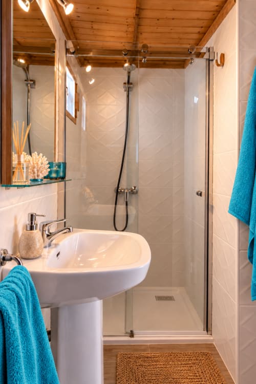 Bagno moderno nell'appartamento Sara & Gino Corralejo con doccia walk-in, lavabo su colonna, asciugamani turchesi e soffitto in legno