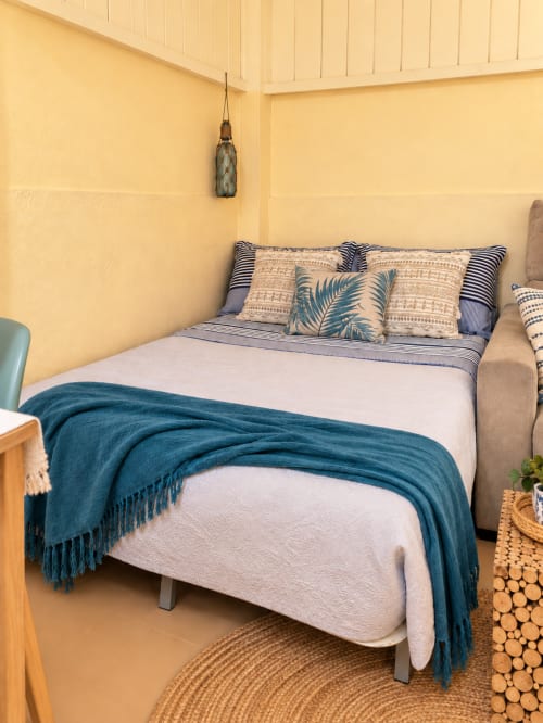 Camera da letto accogliente a Sara & Gino Fuerteventura con biancheria bianca, plaid blu, cuscini decorativi e pareti gialle