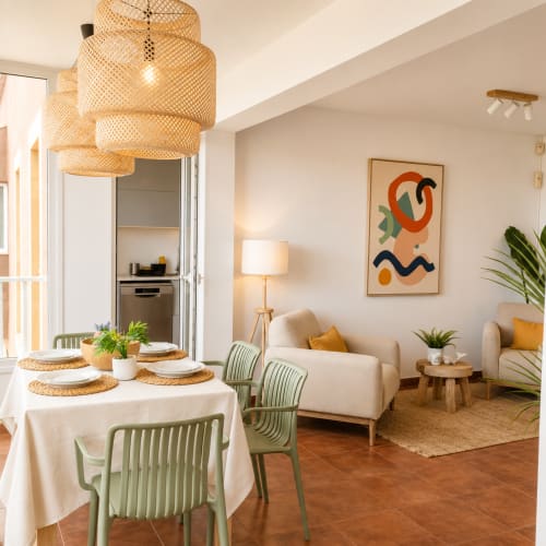 Modern apartment at Sara & Gino Fuerteventura with dining area, woven pendant light, beige sofa, and ocean view in Corralejo