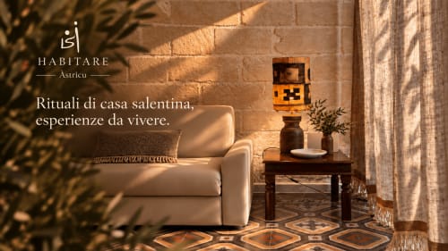Soggiorno accogliente all'HABITARE Astricu di Lecce con poltrona color crema, tavolino in legno, lampada decorativa e dettagli tradizionali