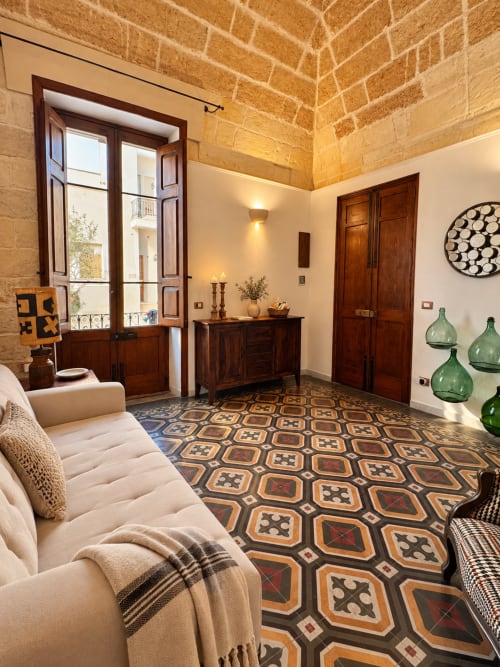 HABITARE Àstricu apartment in Lecce features vaulted brick ceilings, wooden doors, patterned tile floors, cream sofa, and
