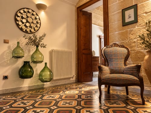 Elegant apartment foyer at HABITARE Lecce with patterned terracotta floor, green glass vases, wooden chair, and decorative