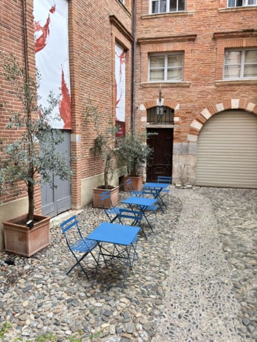 Blauer Außenrestaurantbereich im Innenhof des Les Relais Du Capitole in Toulouse mit Backsteingebäude und Topfpflanzen