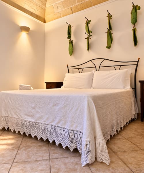Bright bedroom at HABITARE Lecce with wrought iron bed, white linens, wooden beams, and dried peas hanging as decor