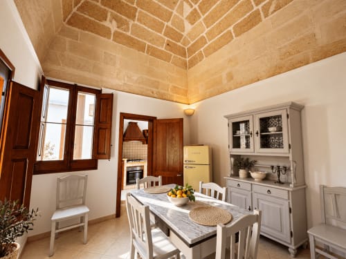 Bright dining area in HABITARE Lecce apartment with exposed wooden ceiling, white table, and cream cabinetry