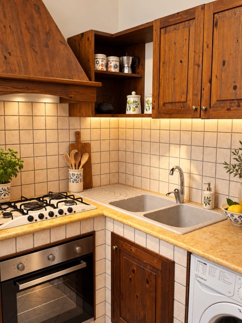 Compact rustic kitchen in HABITARE Àstricu apartment, Lecce with wooden cabinets, cream tiles, gas stove, and double sink