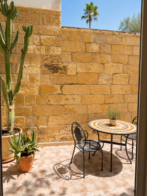 Private patio at HABITARE Lecce with stone walls, mosaic table, seating, and potted cacti in Lecce, Italy