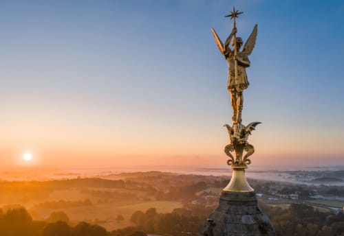 Statue d'ange doré dominant la vallée brumeuse de Pouzauges à l'aube, vue du Petit Moulin